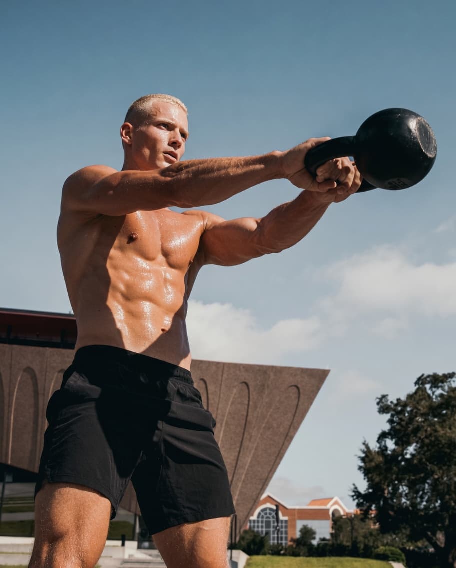 Man mid-kettlebell swing outdoors under a blue sky